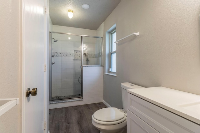 bathroom with toilet, a textured ceiling, wood finished floors, a shower stall, and a textured wall