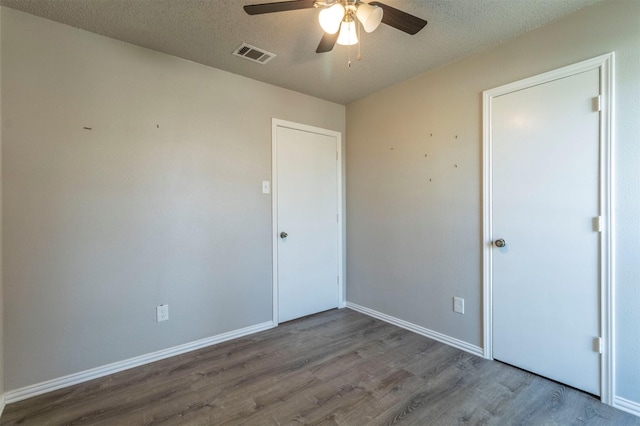 empty room featuring a textured ceiling, wood finished floors, visible vents, and ceiling fan