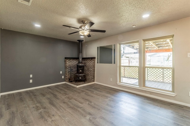 unfurnished living room with baseboards, wood finished floors, ceiling fan, and a wood stove