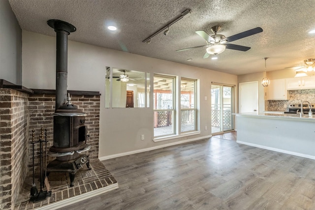 unfurnished living room with a ceiling fan, wood finished floors, a wood stove, a sink, and a textured ceiling