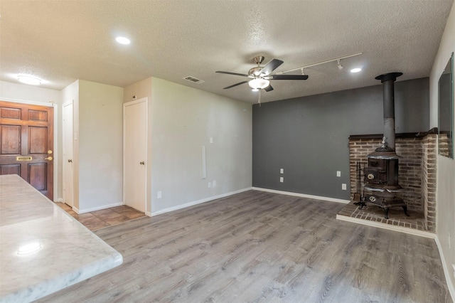 unfurnished living room featuring visible vents, a wood stove, wood finished floors, a textured ceiling, and a ceiling fan