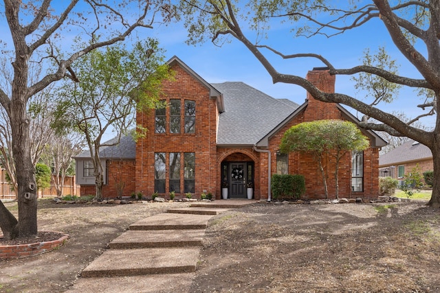 traditional home with a chimney, brick siding, and a shingled roof