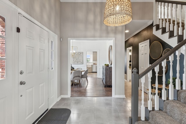 tiled entryway featuring baseboards, a high ceiling, an inviting chandelier, and stairs