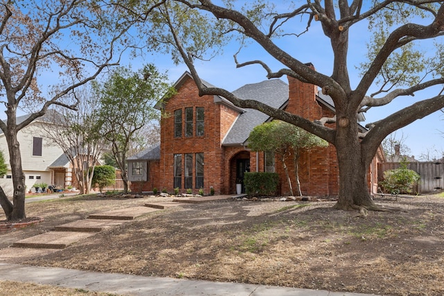 traditional home featuring brick siding, a shingled roof, a chimney, and fence