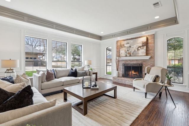 living room featuring visible vents, a brick fireplace, crown molding, and a decorative wall