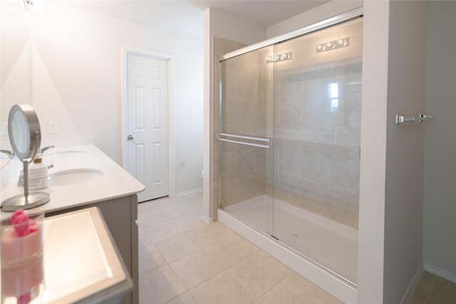full bath featuring tile patterned flooring, a stall shower, baseboards, and double vanity