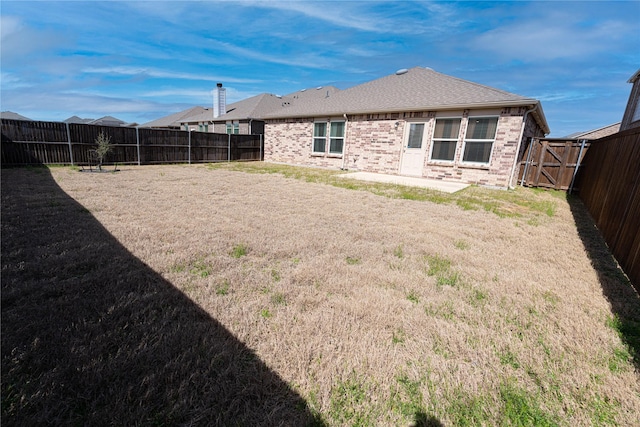 rear view of property with a yard, brick siding, a fenced backyard, and a shingled roof