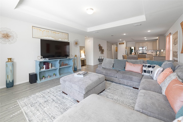 living room with visible vents, a tray ceiling, recessed lighting, light wood finished floors, and baseboards