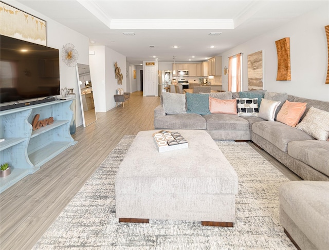 living area with recessed lighting, crown molding, a tray ceiling, and light wood-style floors
