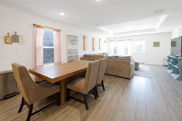dining area with a wealth of natural light, a tray ceiling, visible vents, and light wood finished floors