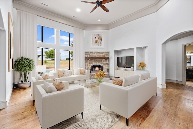 2933 N Star Dr, Celina, TX 75009 - living room featuring arched walkways, light wood-style floors, a stone fireplace, crown molding, and ceiling fan