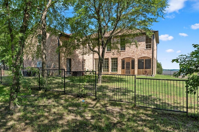 rear view of house featuring a lawn, brick siding, and fence