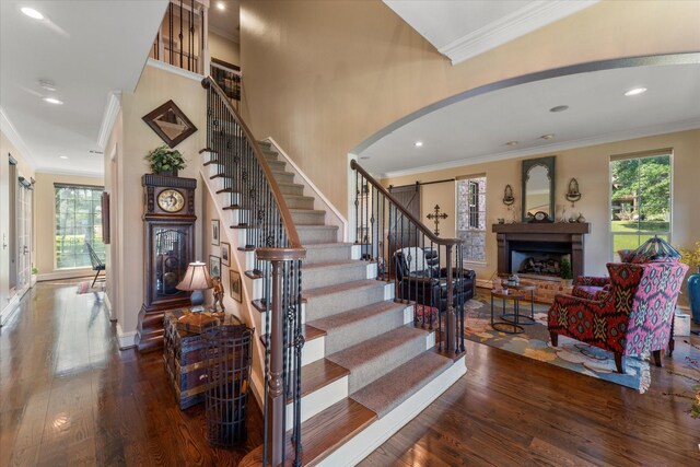 stairs with arched walkways, a fireplace with raised hearth, crown molding, and hardwood / wood-style flooring
