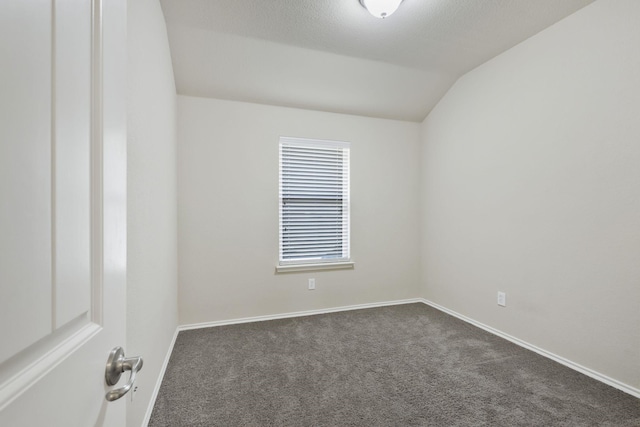 empty room with lofted ceiling, baseboards, and dark carpet