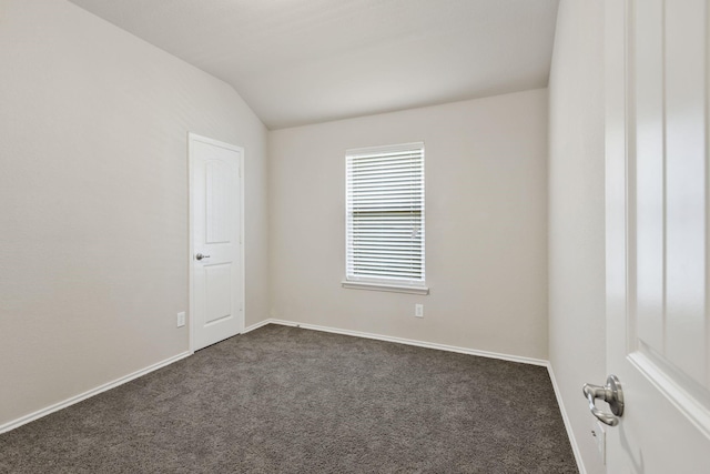 spare room featuring lofted ceiling, dark colored carpet, and baseboards