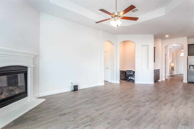 unfurnished living room with arched walkways, a glass covered fireplace, light wood-style flooring, a ceiling fan, and recessed lighting