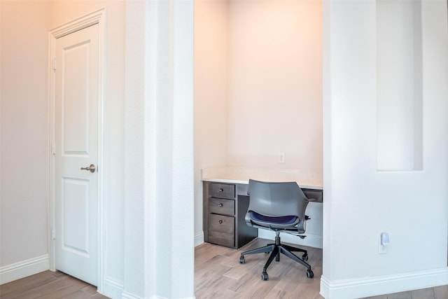 office with baseboards, light wood finished floors, and built in desk