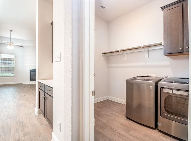 laundry area featuring a ceiling fan, washing machine and dryer, light wood finished floors, and cabinet space