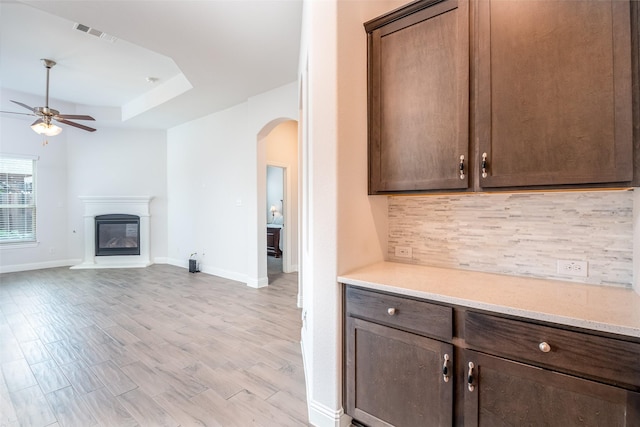 kitchen featuring backsplash, a ceiling fan, visible vents, arched walkways, and dark brown cabinets