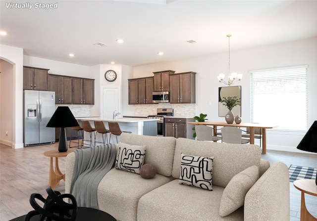 living area with recessed lighting, baseboards, an inviting chandelier, and light wood-style flooring