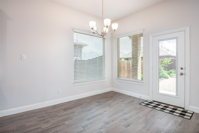 unfurnished dining area with baseboards, wood finished floors, and a notable chandelier