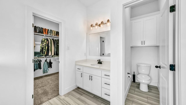 bathroom with vanity, toilet, baseboards, and a walk in closet