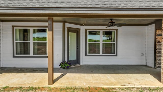 view of exterior entry with roof with shingles, ceiling fan, and a patio