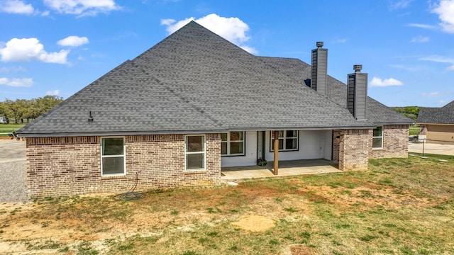 back of property with a patio, a shingled roof, a yard, a chimney, and brick siding