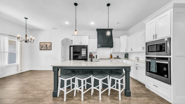 kitchen featuring a sink, decorative backsplash, light countertops, arched walkways, and appliances with stainless steel finishes