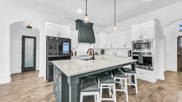 kitchen featuring arched walkways, custom range hood, appliances with stainless steel finishes, light countertops, and white cabinetry