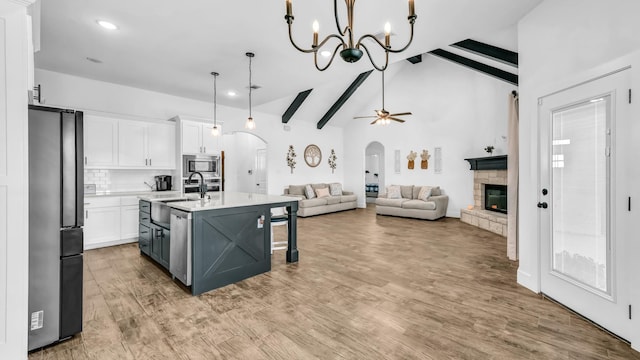 kitchen featuring appliances with stainless steel finishes, white cabinets, beamed ceiling, and arched walkways