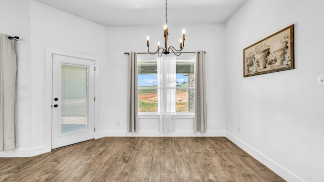 unfurnished dining area with wood finished floors, a chandelier, and baseboards