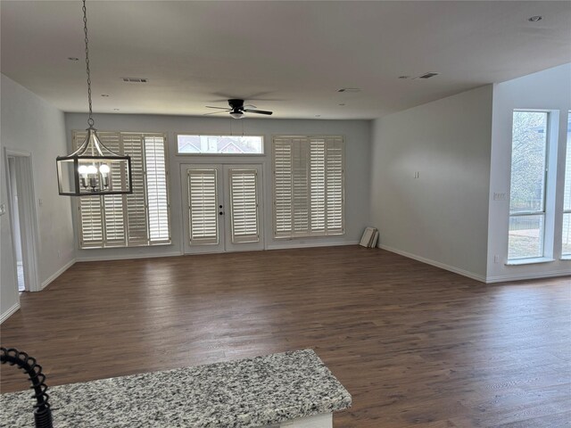 unfurnished living room featuring dark wood-type flooring, ceiling fan with notable chandelier, and baseboards
