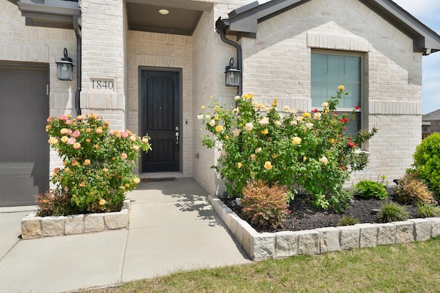 view of exterior entry with an attached garage and brick siding