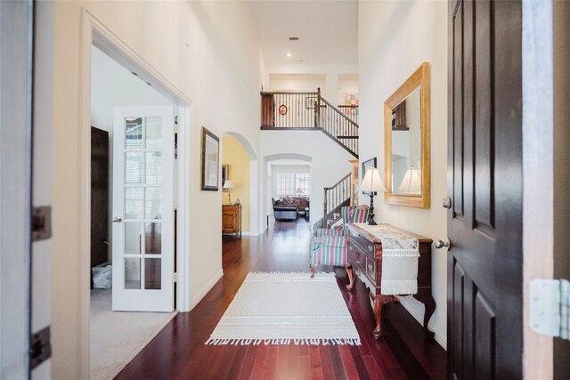 hallway featuring arched walkways, stairs, baseboards, wood finished floors, and a towering ceiling