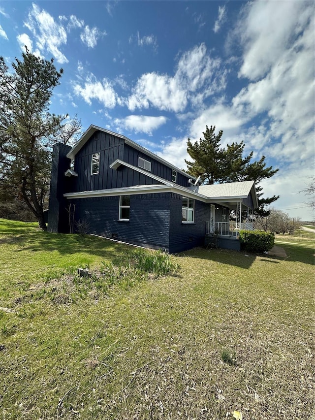view of side of property with brick siding, a yard, covered porch, and board and batten siding