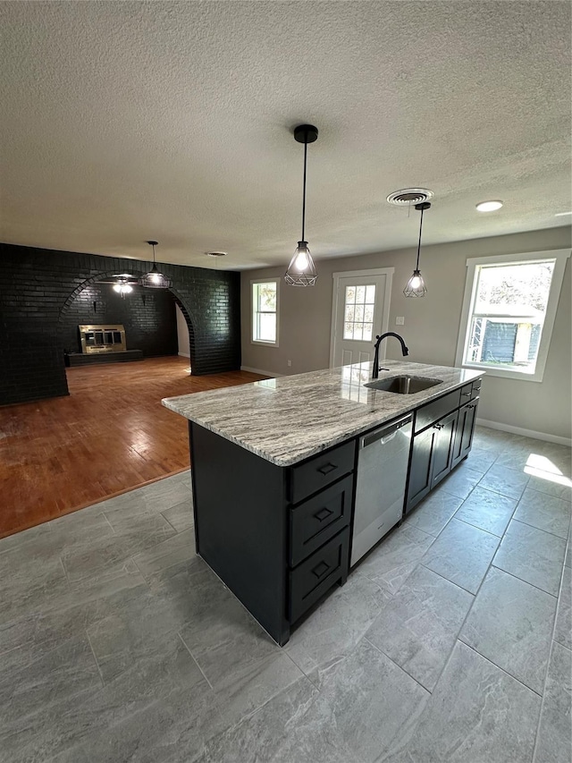 kitchen featuring stainless steel dishwasher, a healthy amount of sunlight, a kitchen island with sink, and a sink