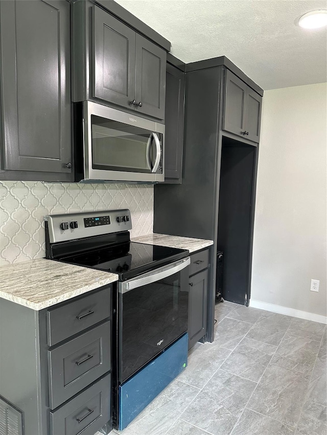 kitchen featuring stainless steel appliances, baseboards, gray cabinets, and decorative backsplash