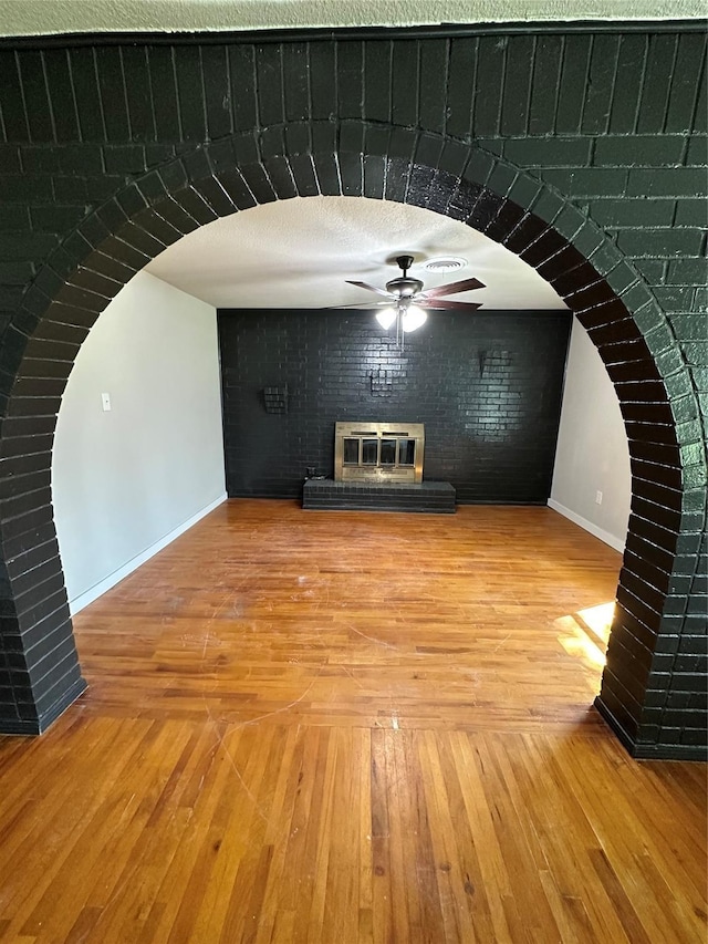 unfurnished living room featuring a ceiling fan, light wood-style floors, brick wall, baseboards, and a brick fireplace