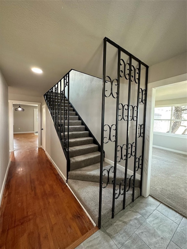 stairway featuring a textured ceiling, carpet, and baseboards