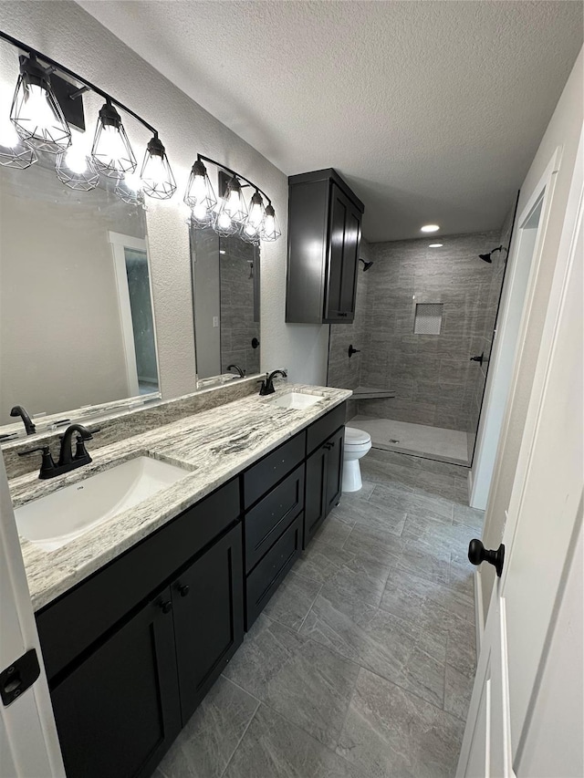 bathroom featuring a sink, toilet, a textured ceiling, and a tile shower