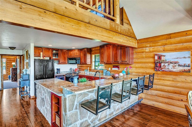 kitchen featuring dark wood-style flooring, light stone counters, black appliances, a peninsula, and log walls