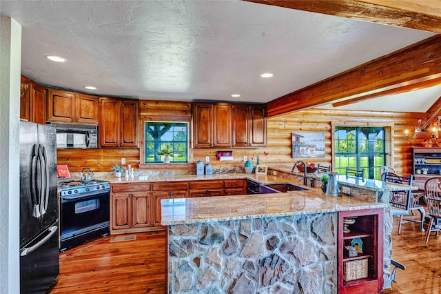 kitchen featuring a sink, log walls, black appliances, and a healthy amount of sunlight