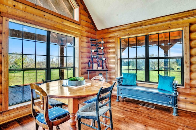 dining room with visible vents, log walls, vaulted ceiling, and wood-type flooring