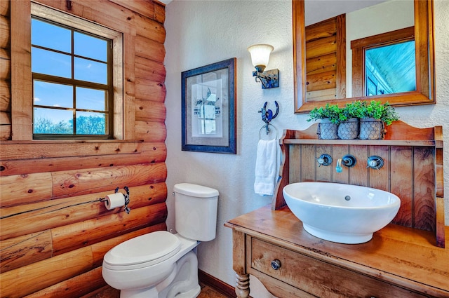 half bath featuring vanity, a textured wall, rustic walls, toilet, and baseboards