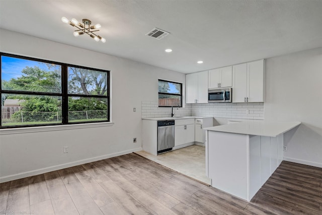 4630 Harvey Dr, Mesquite, TX 75150 - kitchen featuring appliances with stainless steel finishes, a peninsula, decorative backsplash, a sink, and white cabinetry