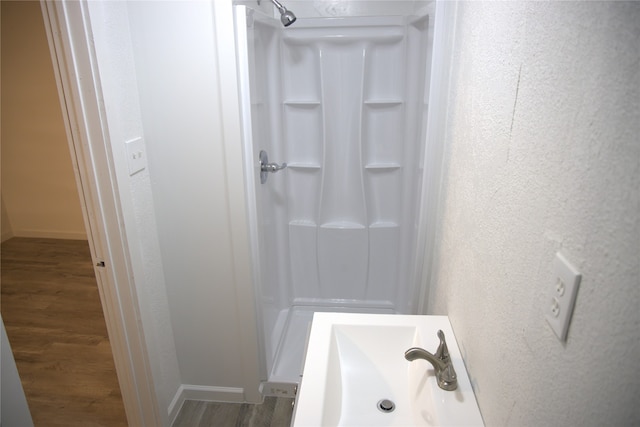 full bathroom featuring a textured wall, wood finished floors, baseboards, walk in shower, and a sink