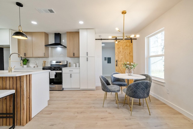 kitchen featuring stainless steel gas stove, a sink, a barn door, wall chimney exhaust hood, and light countertops