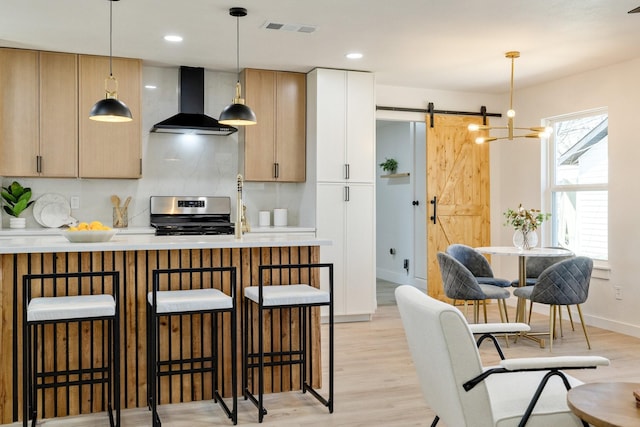 kitchen with visible vents, wall chimney range hood, light wood-style flooring, a kitchen breakfast bar, and gas stove
