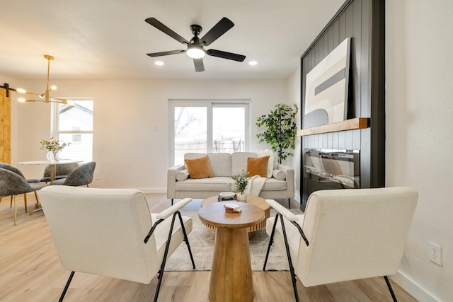 living room featuring recessed lighting, light wood-style flooring, ceiling fan with notable chandelier, and baseboards